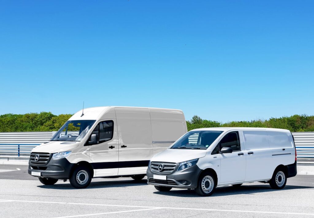 pexels photo 4620555 Two white delivery vans parked in a spacious parking lot under a clear blue sky.